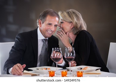Cheerful Woman Whispering Something In Man's Ear In A Elegant Restaurant