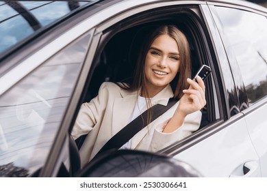 A cheerful woman in a white blazer is sitting inside a car, smiling and holding car keys. The scene conveys excitement and independence, highlighting modern transportation and personal achievement. - Powered by Shutterstock