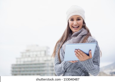 Cheerful Woman With Winter Clothes On Using Her Tablet Outdoors On A Cold Grey Day