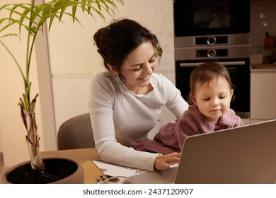 Cheerful woman working at home with her little child daughter - Powered by Shutterstock