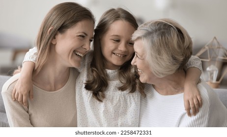 Cheerful women and kid of three different female generations meeting on home couch, hugging with love, affection, talking, chatting, laughing, enjoying family leisure, relations, bonding, having fun - Powered by Shutterstock