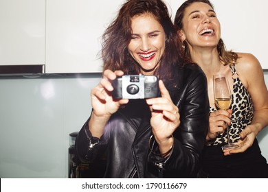 Cheerful Women Partying At Home Drinking Wine. Woman Taking A Photo On A Disposable Camera At A House Party.