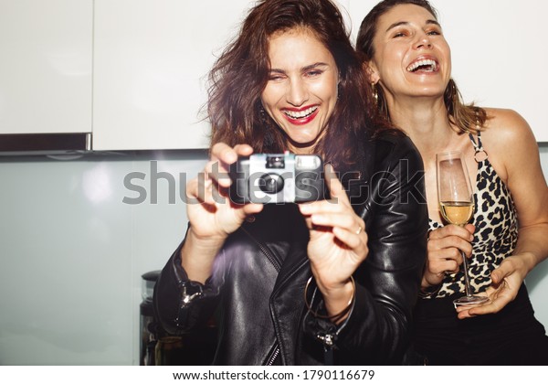 Cheerful women\
partying at home drinking wine. Woman taking a photo on a\
disposable camera at a house\
party.