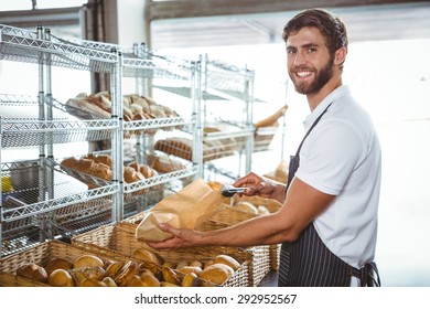 Cheerful worker standing and presenting a bread at the bakery