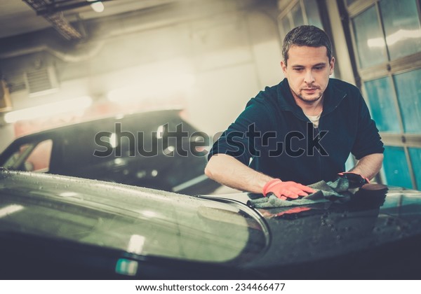 Cheerful worker wiping\
car on a car wash