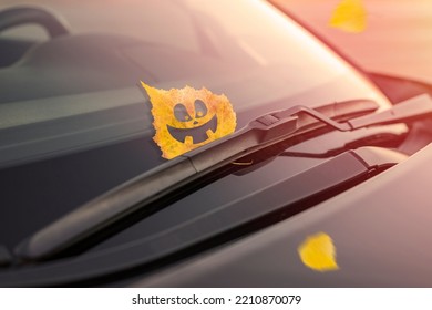 Cheerful yellow leaf with emotion, on the windshield of the car under the brush. Concept of warm autumn or Halloween holiday. Toned background