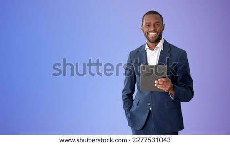 Cheerful young African American businessman holding tablet computer over purple background. Concept of social media. Mock up
