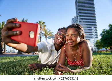 A cheerful young African American couple taking a selfie portrait with their smart phone lying on the grass in the city park. Smiling boy and girl using cell. Black people lovers outdoors. - Powered by Shutterstock