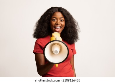 Cheerful Young African American Female Making Announcement With Loudspeaker, Excited Black Millennial Woman Holding Megaphone In Hands, Sharing News While Standing Over White Background, Copy space