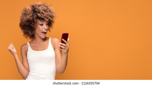 Cheerful young african american girl using mobile phone,smiling, posing on yellow background.