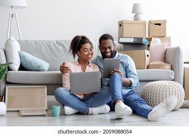Cheerful young african american lady and guy relaxing on couch using tablet for buying furniture online in room with cardboard boxes. Interior design planning, renovation, searching idea for new flat - Shutterstock ID 2059088054
