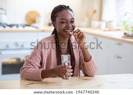 Cheerful Young African American Lady Taking Beauty Supplement Pill In Kitchen, Happy Black Millennial Woman Sitting At Tablet, Eating Multivitamin Tablet And Drinking Water At Home, Free Space