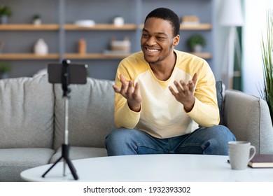 Cheerful Young African American Man Influencer Broadcasting From Home, Using Smartphone And Tripod, Copy Space. Smiling Black Guy Vlogger Talking At Mobile Phone Camera, Shooting Video For Followers