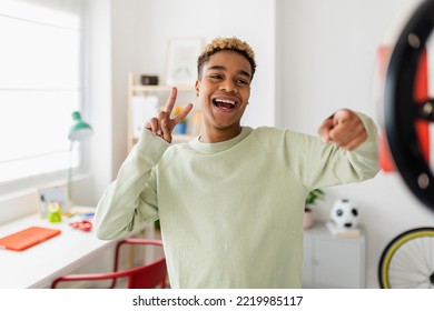 Cheerful young african american teenage boy recording video for social media. Millennial content creator male student having fun streaming online using mobile phone network app from domestic room - Powered by Shutterstock