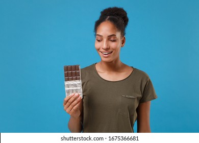 Cheerful young african american woman girl in casual t-shirt posing isolated on bright blue wall background studio portrait. People emotions lifestyle concept. Mock up copy space. Hold chocolate bar