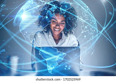 Cheerful young African American woman using laptop in blurry office with double exposure of futuristic network interface and planet hologram. Concept of internet and communication. Toned image - Powered by Shutterstock