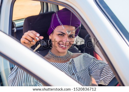 cheerful young african american woman in a purple turban on head showing her new car key at summer beach.indian female person enjoying a new car purchase