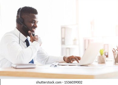 Cheerful Young African Employee With Headset Sitting In Front Of Laptop In Office, Side View, Copy Space