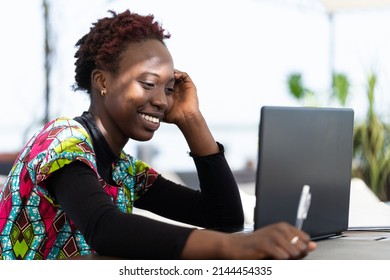 Cheerful Young African Woman Following A Tutorial From Her Favorite Influencer Blogger On Her Laptop, Taking Notes; Global Modern Media Consumption