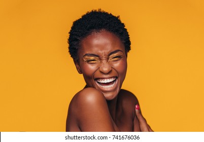 Cheerful young african woman with vivid makeup on her eyes. Female model laughing against yellow background. - Shutterstock ID 741676036