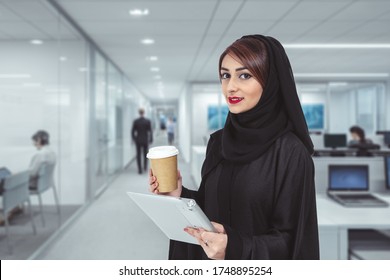 cheerful young Arab business woman in office looking to the camera using tablet and  drinking coffee.