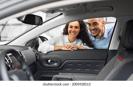 Cheerful Young Arab Man And Woman Buying New Car, Checking Automobile Salon Through The Window. Smiling Middle-eastern Couple Looking Inside Beautiful Black Auto In Showroom, Purchasing Auto