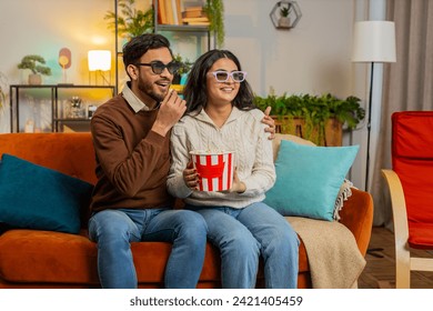 Cheerful young Arabian couple in 3D glasses eating popcorn and watching comedy movie sitting on sofa in living room at home. Smiling diverse family laughing enjoying film during weekend in apartment. - Powered by Shutterstock