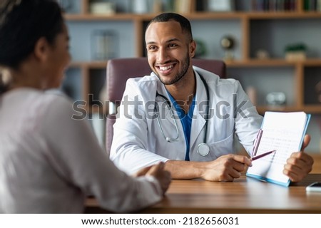 Cheerful young arabic general practitioner showing black lady patient treatment plan, african american woman attending therapist at newest private clinic, modern healthcare concept