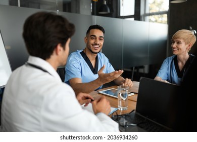 Cheerful young arabic man head physician having team-building with multiracial team of doctors at his office. Professional multiethnic group of male and female healthcare employees having conference