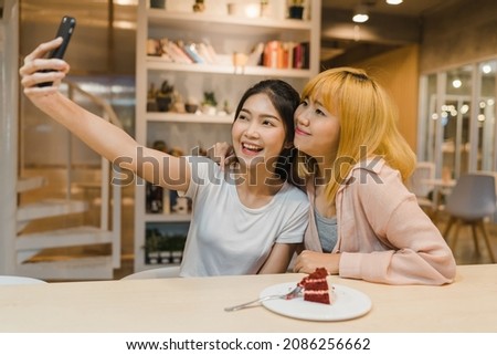 Cheerful young Asia friend clicking selfie using mobile phone at a coffee shop. Two joyful attractive Asian girls together at restaurant or cafe. Holiday activity, or modern lifestyle concept.