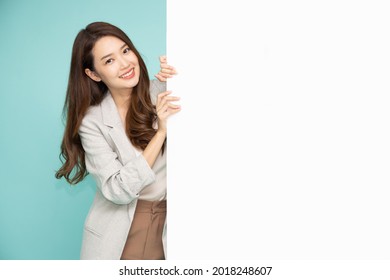 Cheerful Young Asian businesswoman is standing behind the white blank banner or empty copy space advertisement board on green background, Looking at camera - Powered by Shutterstock