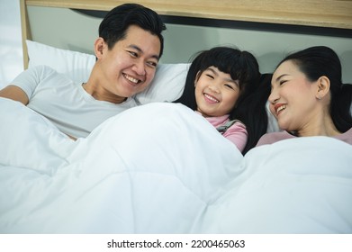 Cheerful Young Asian Family Of Handsome Father And Beautiful Mother Lying On Bed With Cute Little Daughter Laughing While Watching A Comedy Movie On Laptop And Relaxing At Home