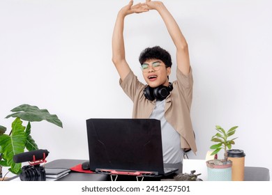 A cheerful young Asian graphic designer stretches joyfully during a work break in a well-organized creative space. - Powered by Shutterstock