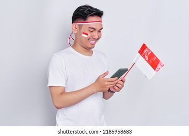 Cheerful young Asian man using mobile phone and celebrating Indonesia independence day on August 17 isolated on white background - Shutterstock ID 2185958683