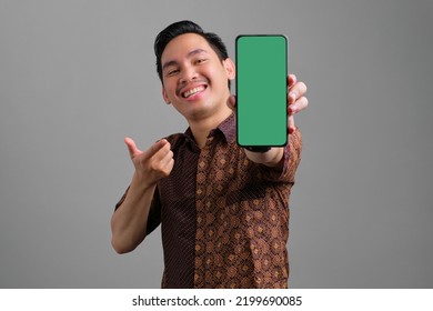 Cheerful Young Asian Man Wearing Batik Shirt Showing Blank Screen Smartphone Isolated On Grey Background
