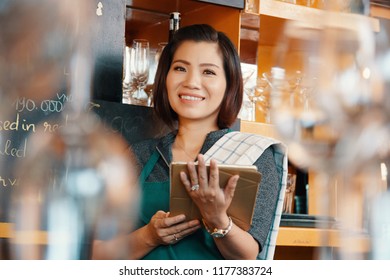 Cheerful young Asian waitress with digital tablet standing behind the counter - Shutterstock ID 1177383724