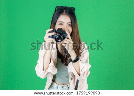 Cheerful young Asian woman with bag and digital camera ready enjoy travel over green isolated background.