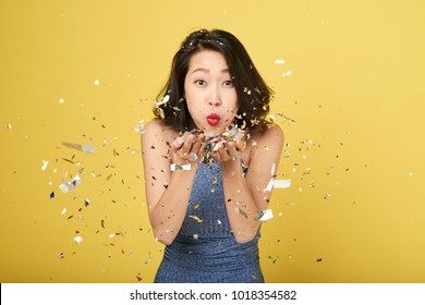 Cheerful Young Asian Woman Blowing Confetti Into Camera