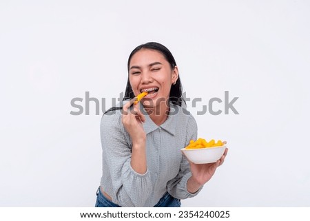 A cheerful young asian woman enjoying a bowl of cheese puffs. Having a delicious snack. Isolated on a white background.