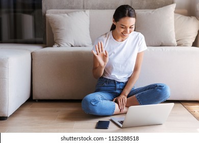 Cheerful Young Asian Woman Having A Videocall While Sitting On A Floor With Laptop Computer