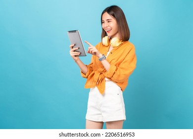 Cheerful young Asian woman in headphones listening to music and enjoy favourite playlist application on digital tablet with dancing on blue background. - Powered by Shutterstock