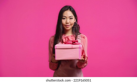 Cheerful Young Asian Woman Holding Wrapped Present Isolated On Pink 