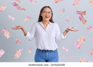 Cheerful young Asian woman rejoicing success with money banknotes flying in the air isolated over white background - Shutterstock ID 2191632209