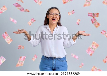 Cheerful young Asian woman rejoicing success with money banknotes flying in the air isolated over white background