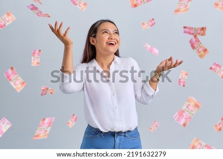 Cheerful young Asian woman rejoicing success with money banknotes flying in the air isolated over white background