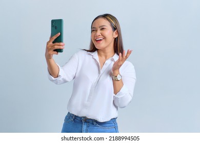 Cheerful Young Asian Woman Saying Hi And Waving Hand While Making Video Call On Mobile Phone Isolated Over White Background