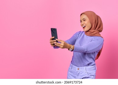 Cheerful young Asian woman taking a selfie with a mobile phone on pink background