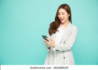 Cheerful young Asian woman using smartphone and receiving good news from the message on mobile chat application isolated over green background