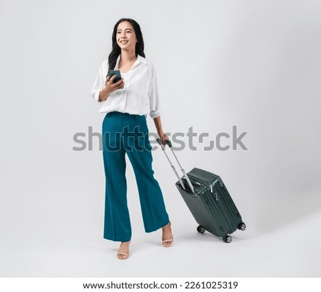 Cheerful young Asian woman using smartphone and holding suitcase with walking to the front, isolated on white background. Concept tourist holiday trip.