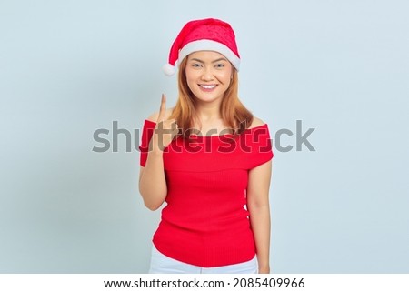 Cheerful young Asian woman wearing christmas dress and pointing up isolated on white background